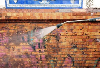 A person using a pressure washer to remove graffiti from a commercial brick wall